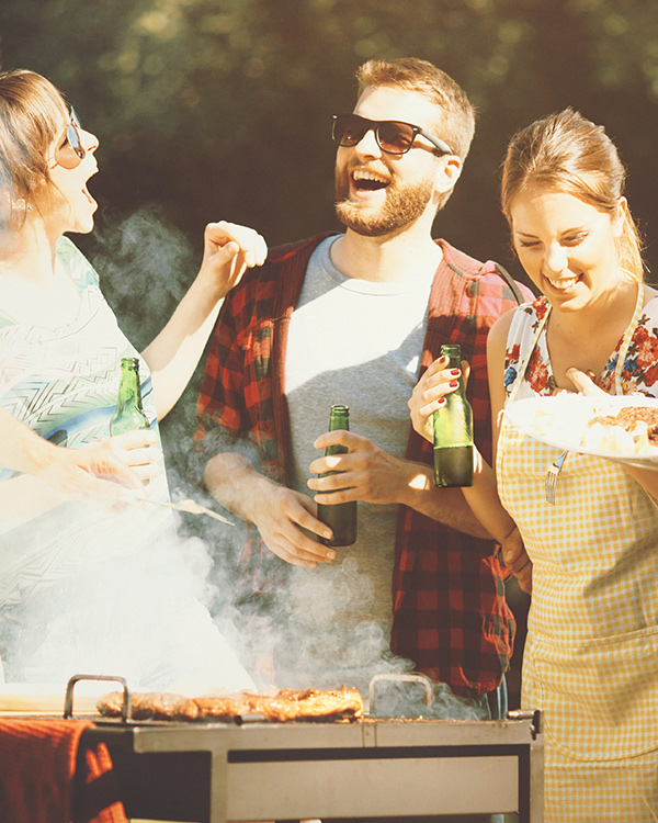 Three friends laugh around a grill on a summer afternoon